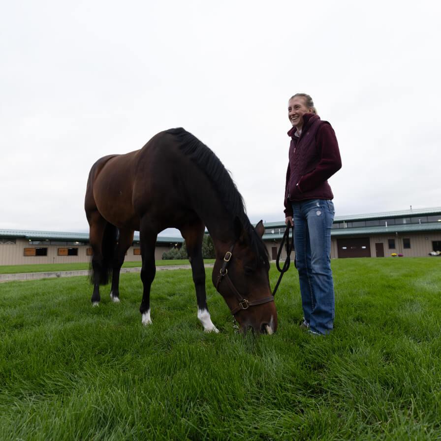 Women standing with horse on lead while it grazes on grass
