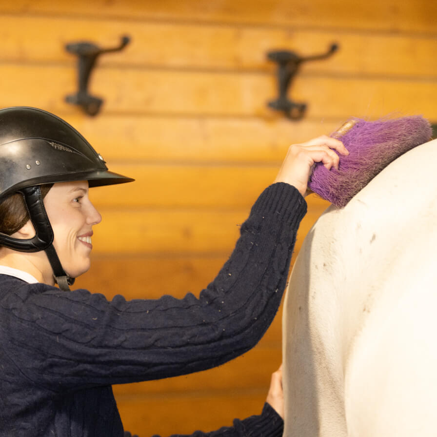 A horse owner caring for her horse, smiles at her horse’s clinical signs of PPID improve after using the Prascend treatment. 